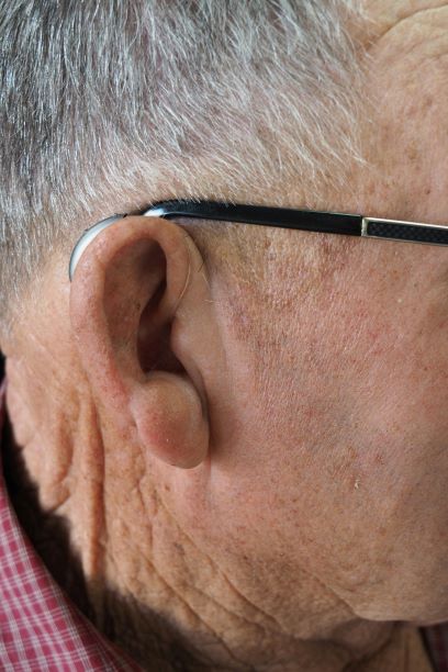A close up image of a person's right ear. This individual is wearing eyeglasses and is using a very smal hearing aid.